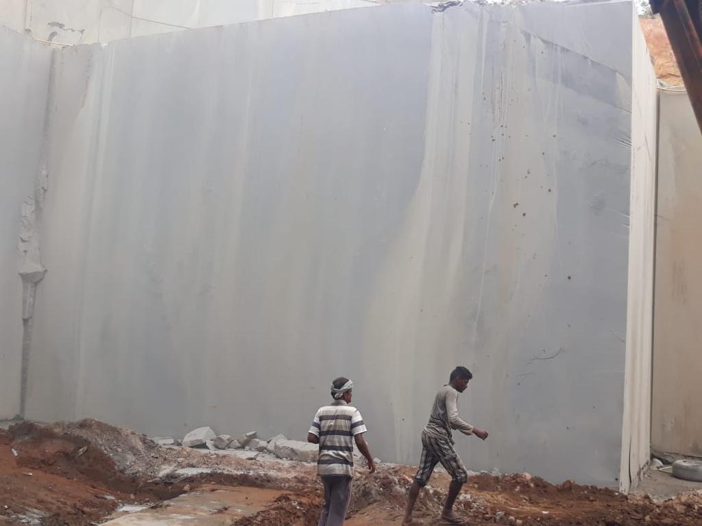 Workers beside a freshly cut white granite quarry wall in South India